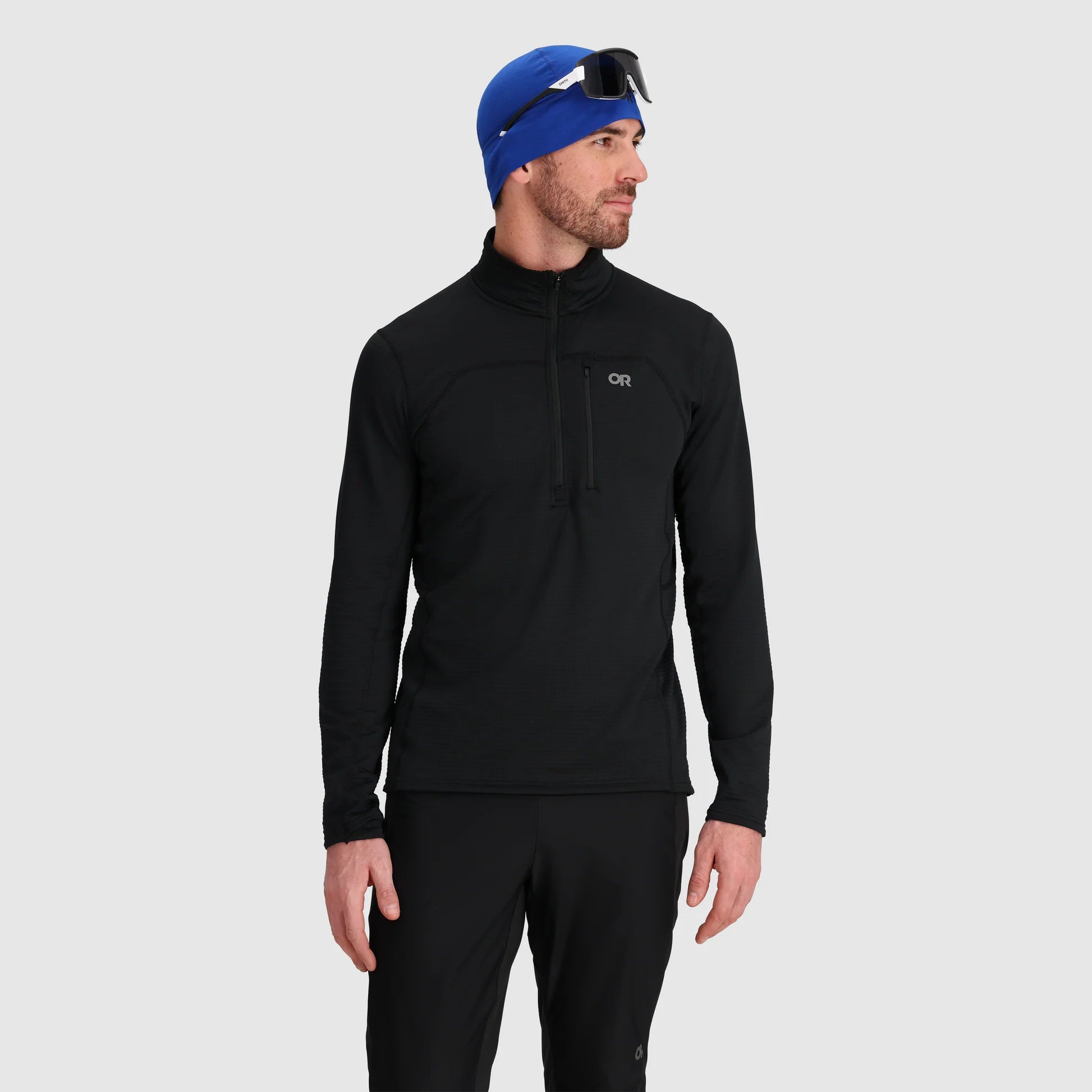 Man wearing a black long-sleeve athletic shirt and blue beanie on a light gray background