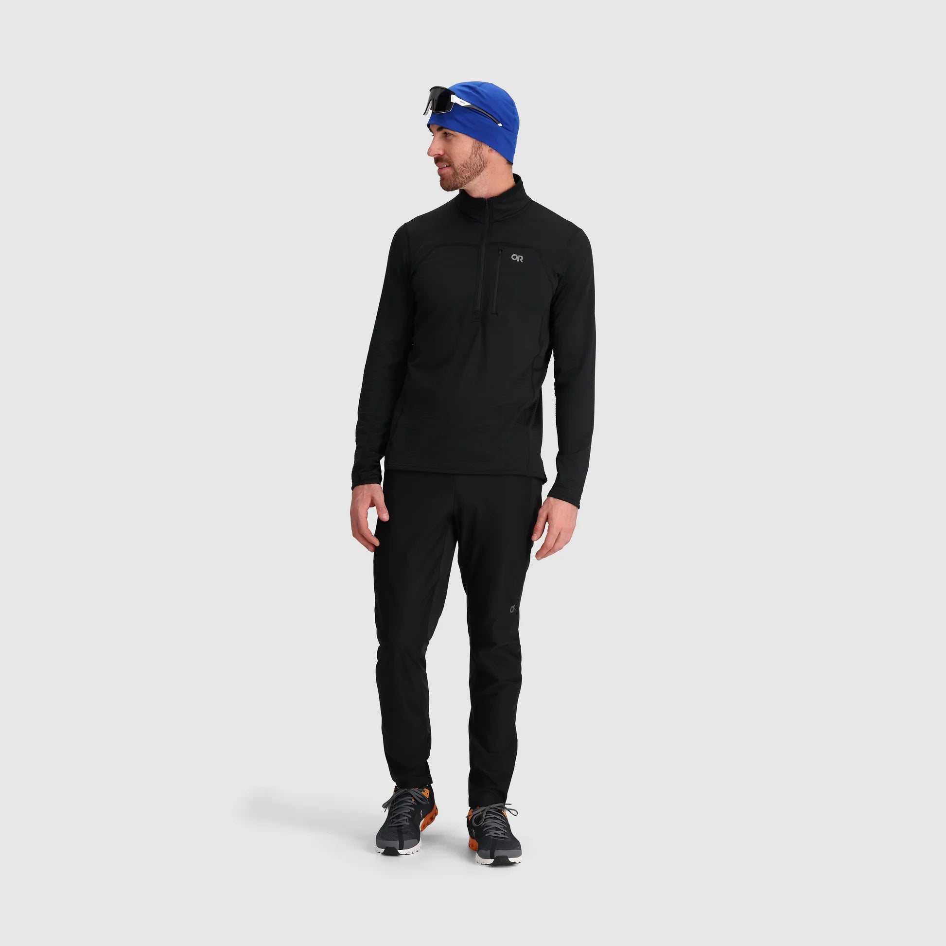 Man wearing a black outfit with a blue beanie on a light gray background