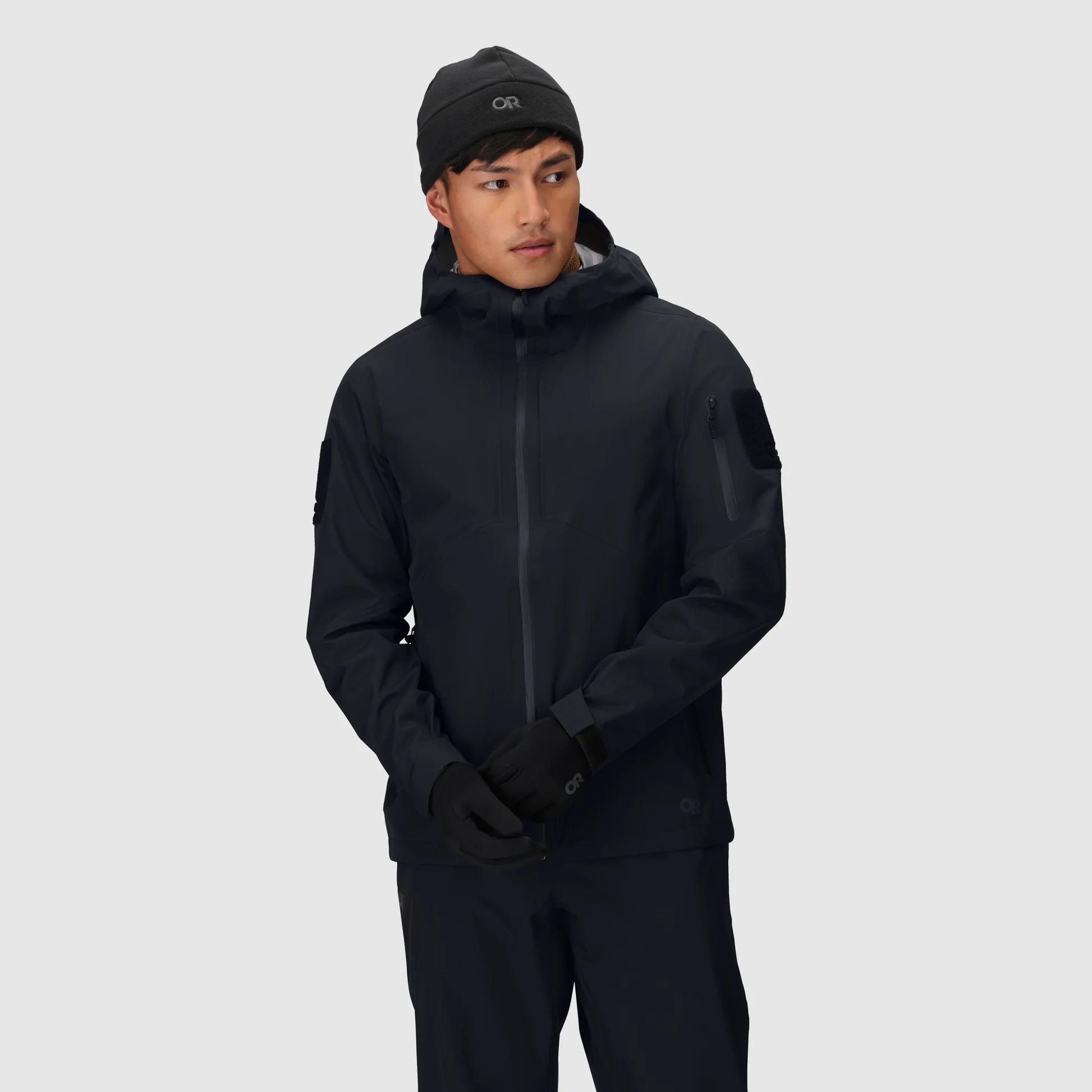 Person wearing a black jacket and pants with a hood on a light gray background