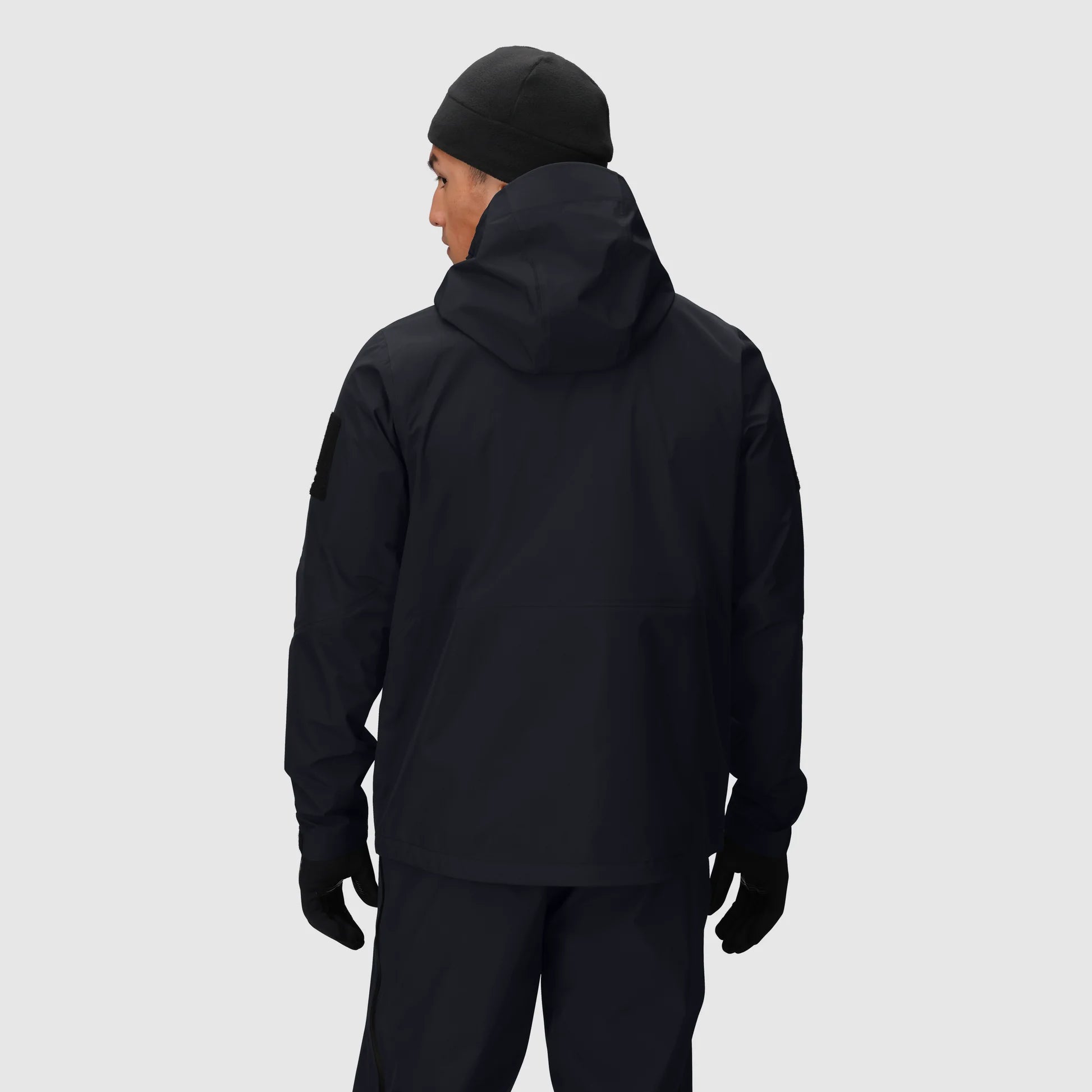 Person wearing a black jacket, pants, and beanie on a light gray background