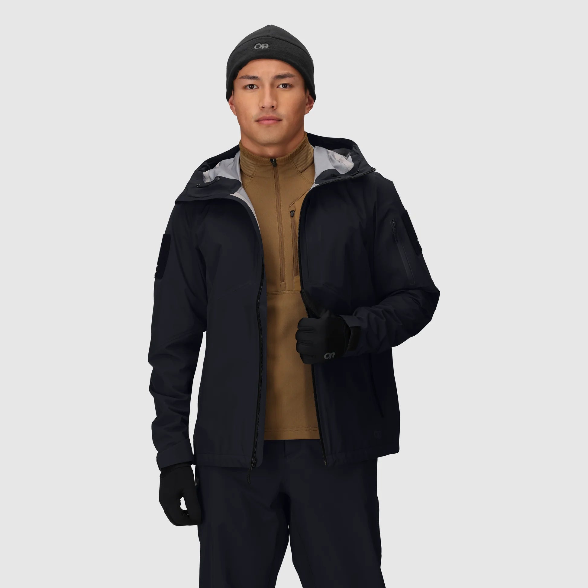 Person wearing a black jacket, brown shirt, and black pants on a light gray background