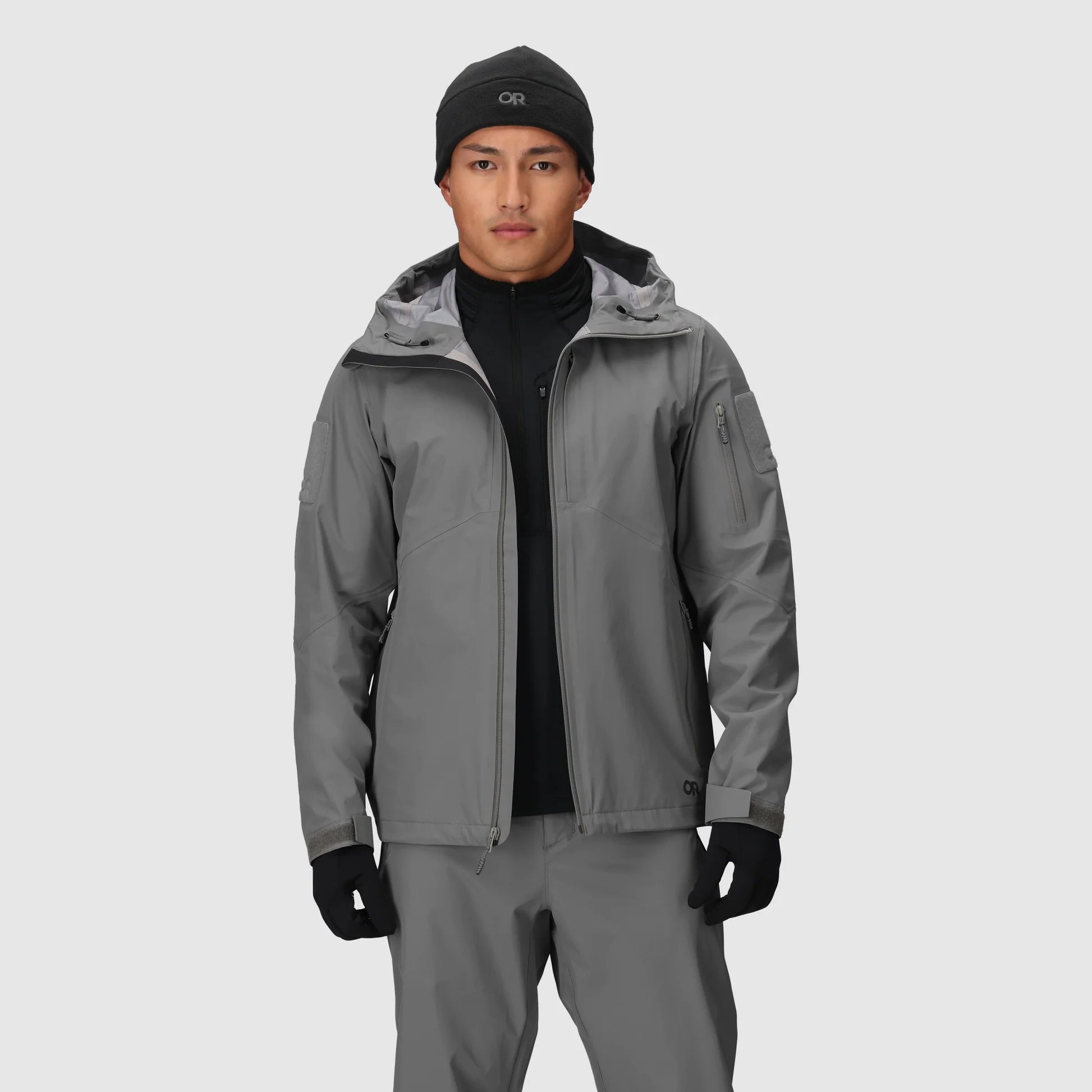 Person wearing a gray jacket, black beanie, and gloves on a light gray background