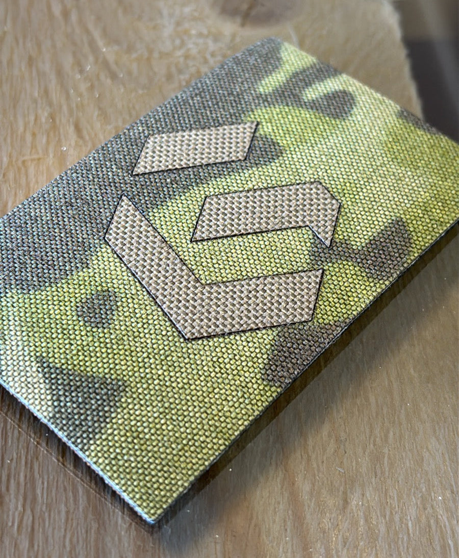 Camouflage patch with a metal V-shaped design on a wooden surface