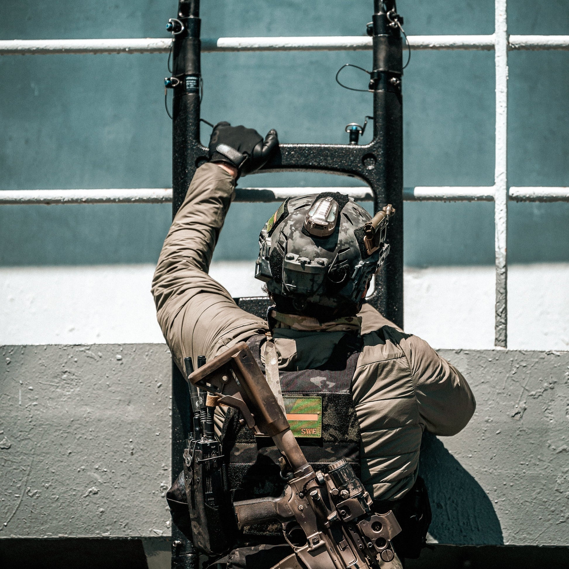 Person in tactical gear climbing a ladder against a striped wall.